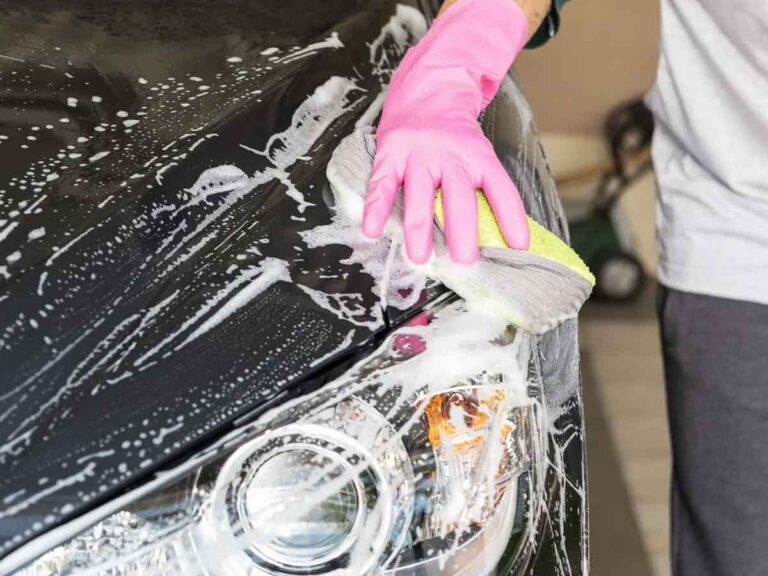close up detail of a person with a pink glove and soapy sponge performing a car washing service