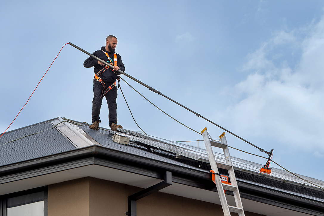 CleanMade technician on a roof using a pole and soft brush to gently wash solar panels