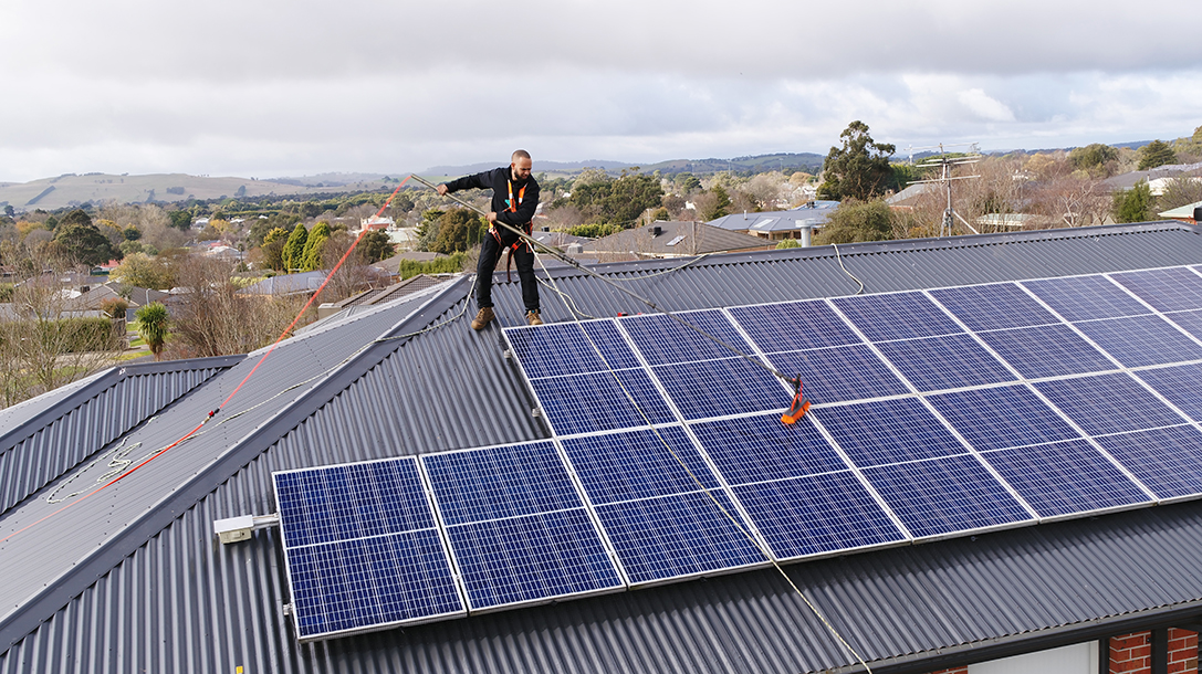 CleanMade technician on a roof using a pole and soft brush to gently wash solar panels