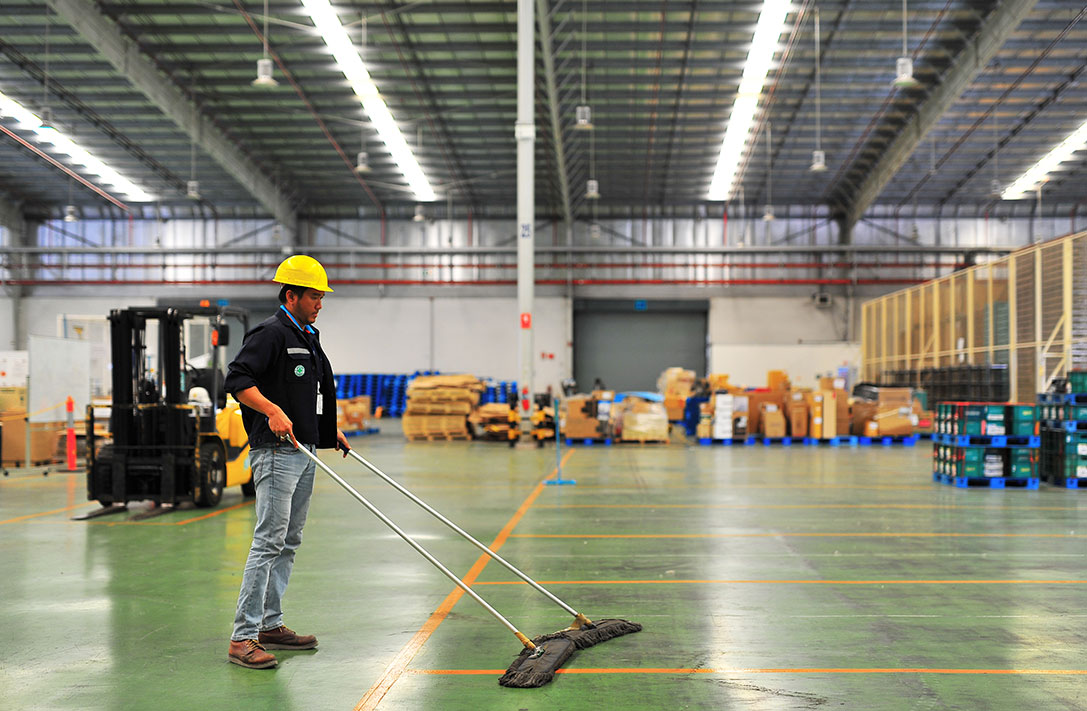 warehouse cleaning with man using a large scissor mop on green concrete floor