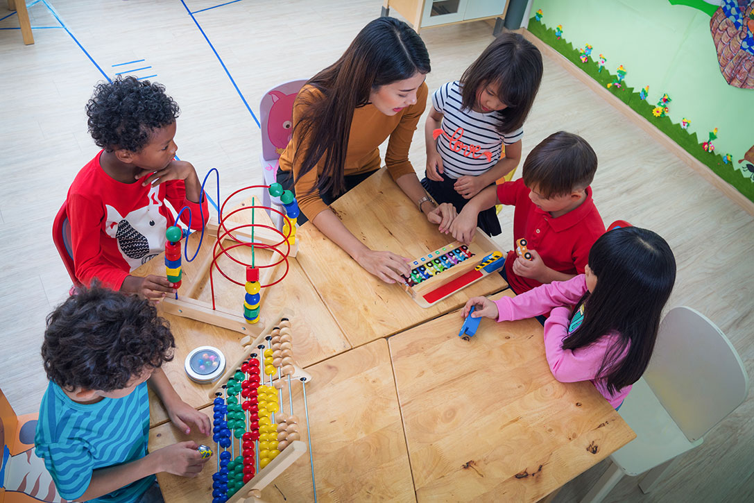 school cleaning service with overhead image of an early childcare worker at table with five children playing with wooden toys