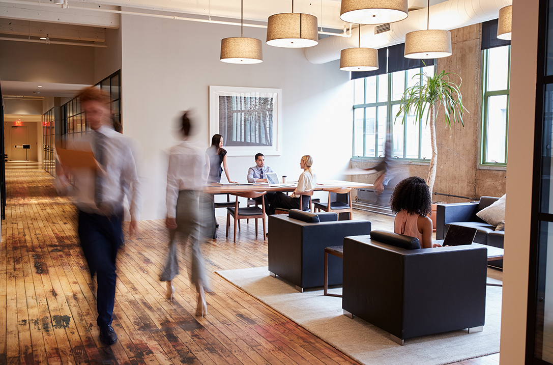 office cleaning with blurred movement of workers walking past while others are seated on leather chairs and a table in an ambient light-filled room