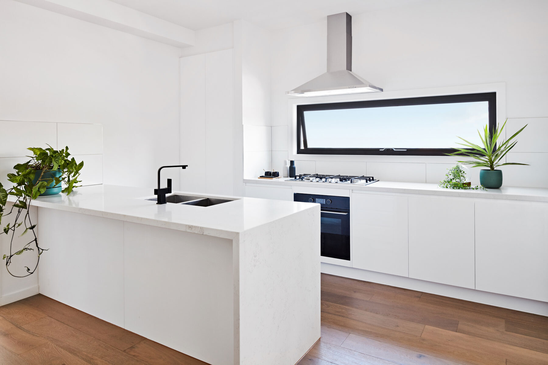 white kitchen with black appliances and rangehood in front of a narrow horizontal window